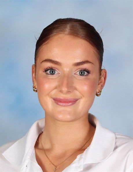 Smiling person in a white collared shirt against a light blue background