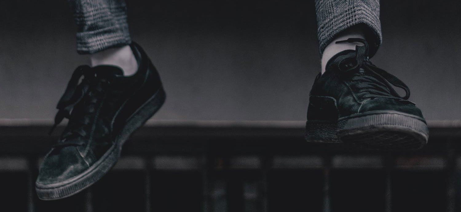 black and white photo of someone sitting on a ledge with their sneakered feet dangling.