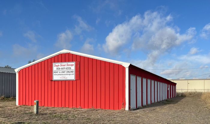 Red metal storage building with white trim and a sign, set on a gravel lot under a blue sky.