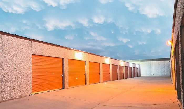 Row of orange storage unit doors in a paved outdoor lot under a blue sky at dusk