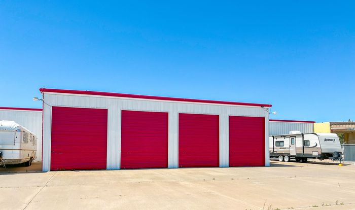 Red warehouse with four garage doors in a sunny industrial lot, with trailers parked on both sides