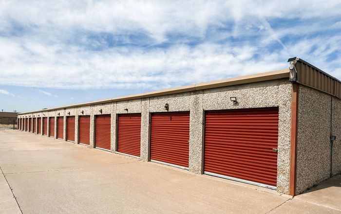 Row of red storage unit doors in a stone-walled self-storage building under a cloudy sky