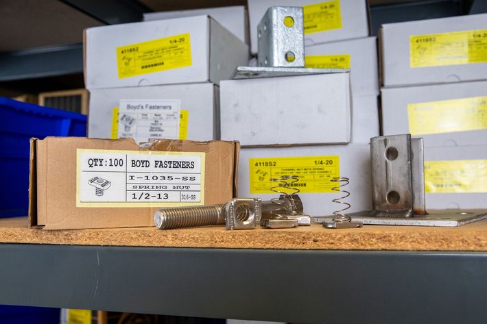 Cardboard box and metal hardware with several boxes on a shelf.