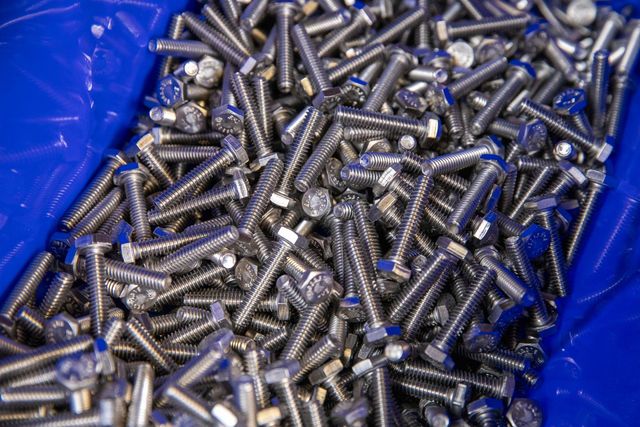 Pile of shiny metal bolts in a blue bin.
