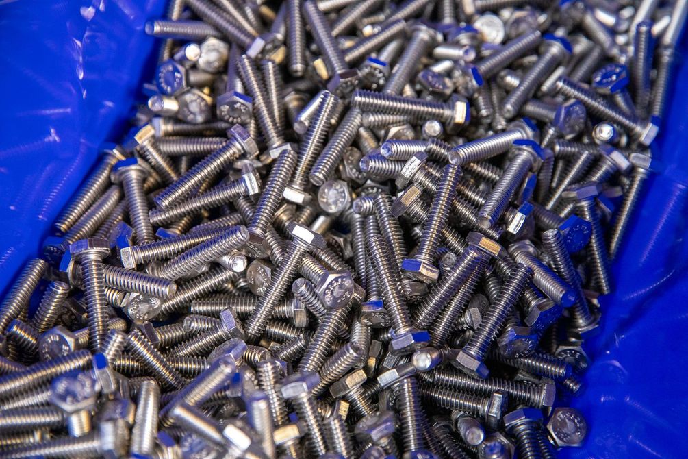 Pile of shiny silver bolts in a blue bin.