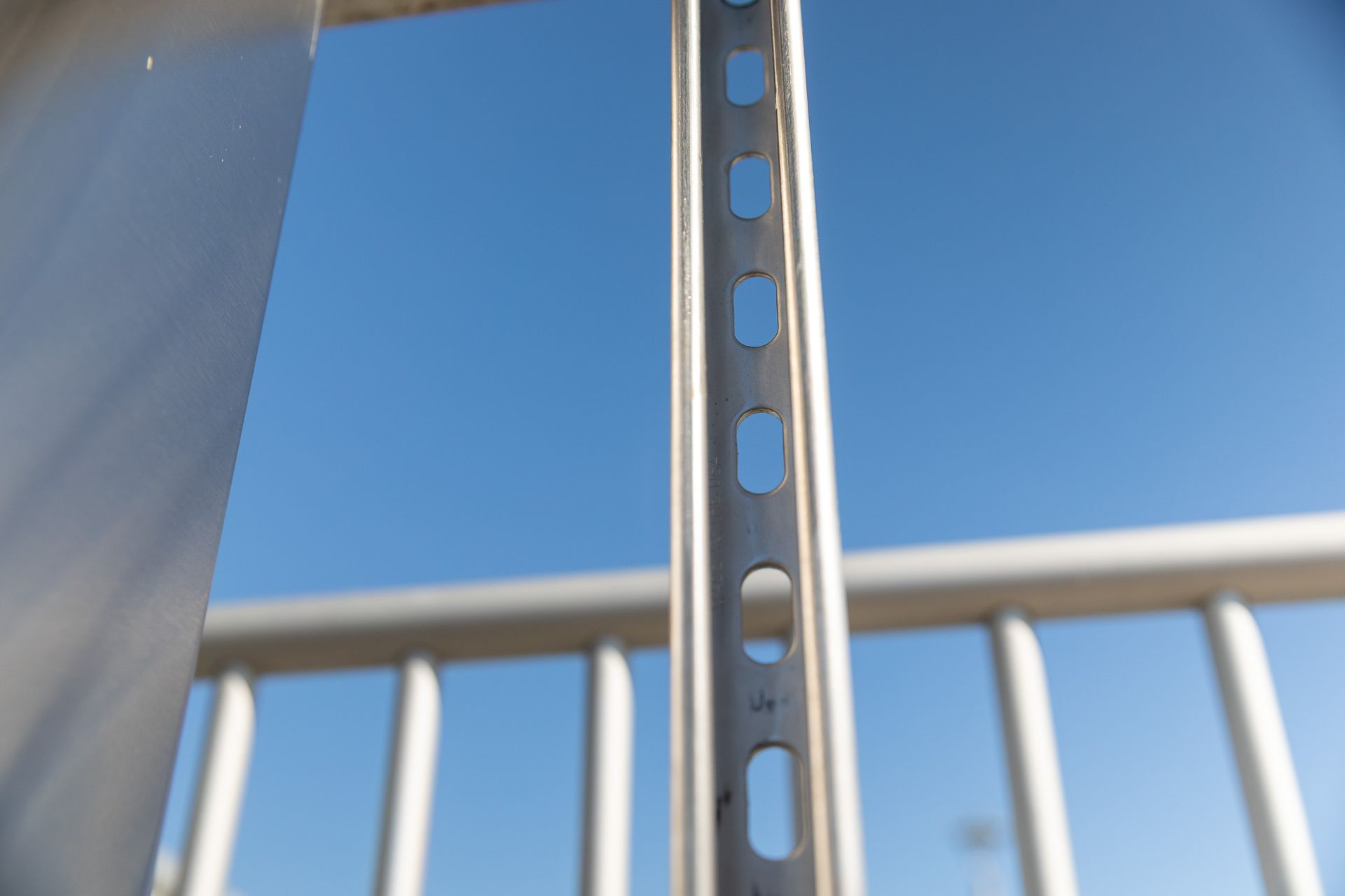 Close-up of a metal railing with a blue sky in the background, showing a slotted metal support.