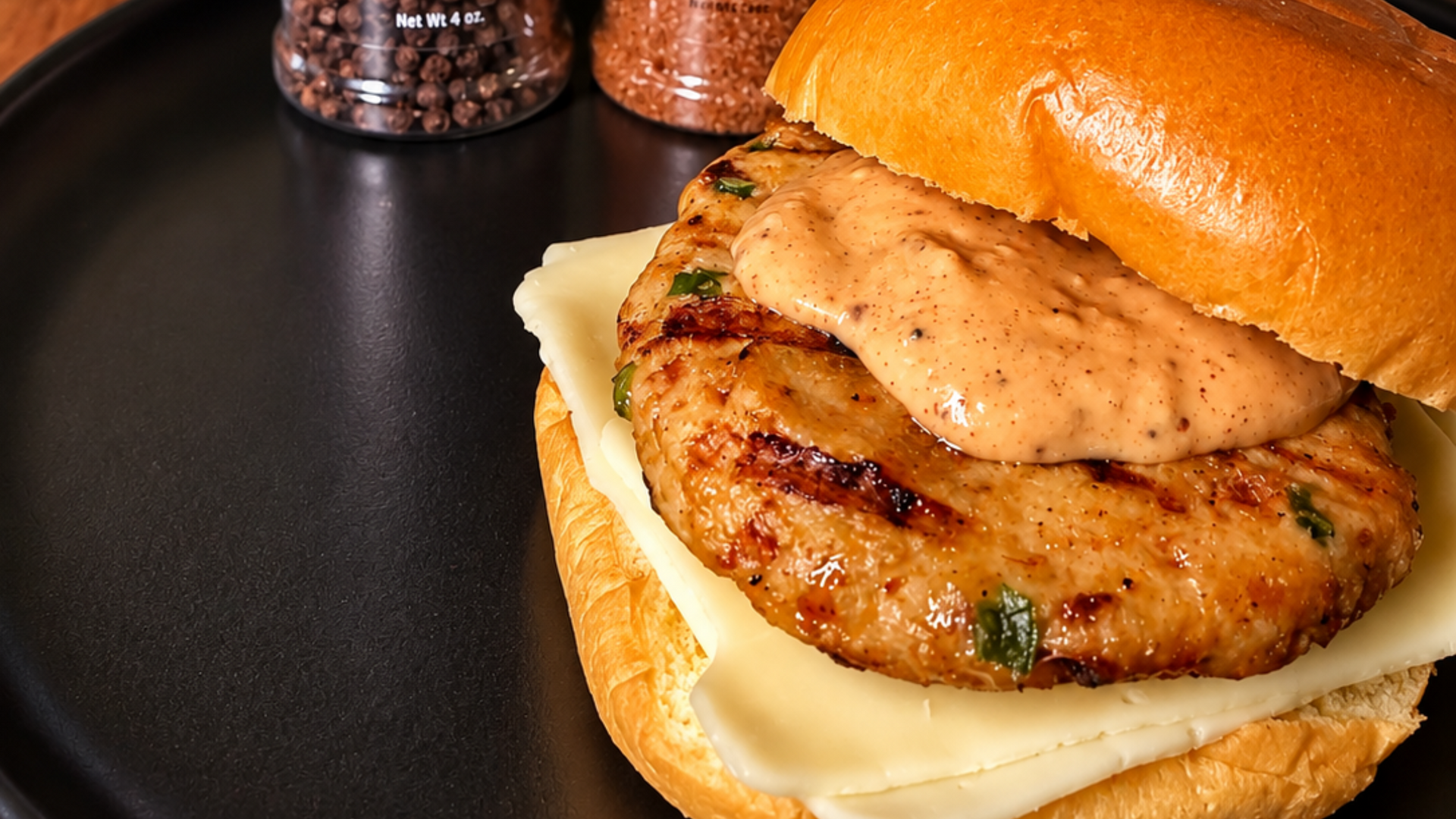 Close-up of a sandwich with grilled chicken and cheese on a bun on a dark surface