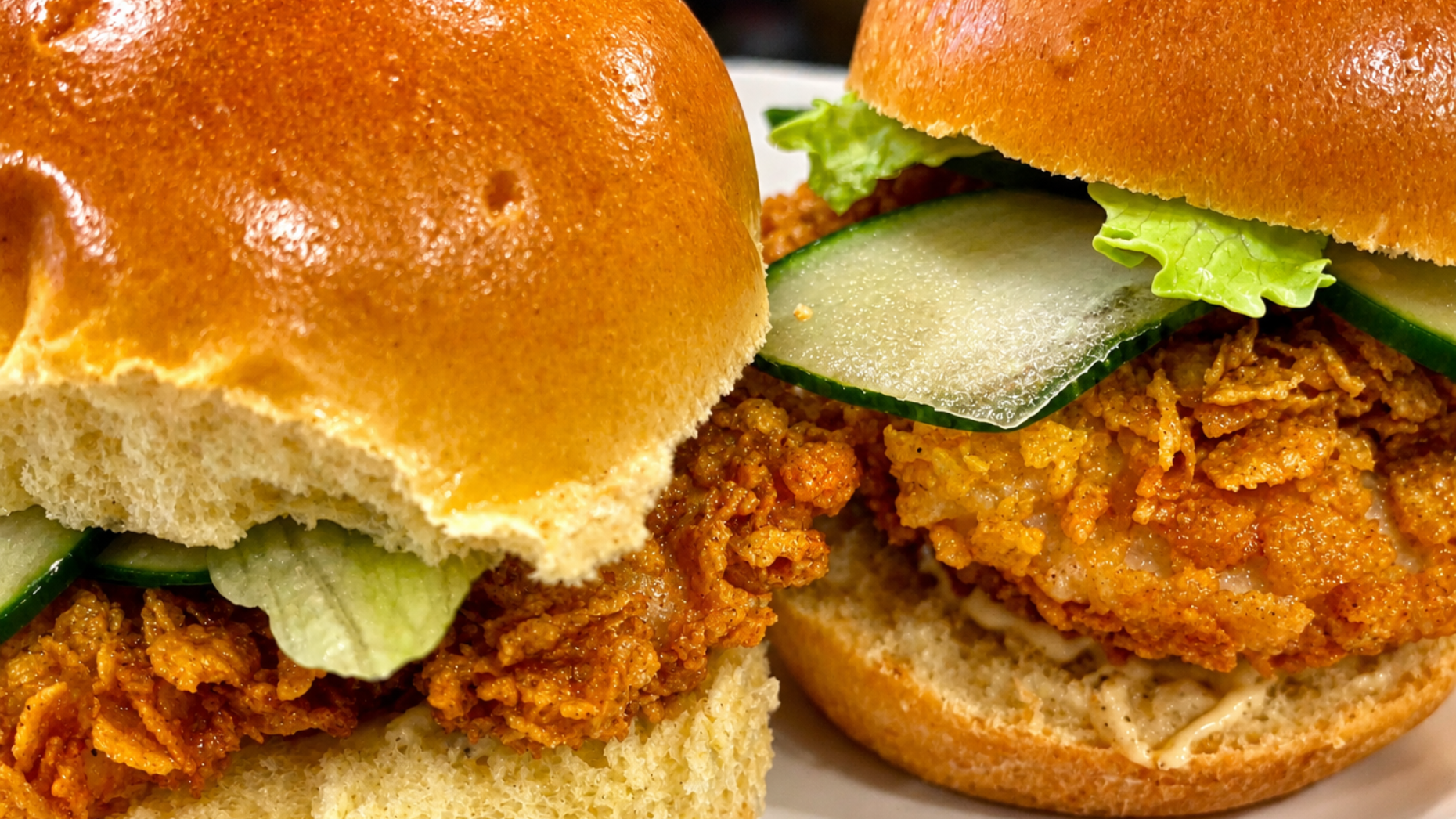 Close-up of two crispy fried chicken sandwiches on shiny buns with lettuce and pickles