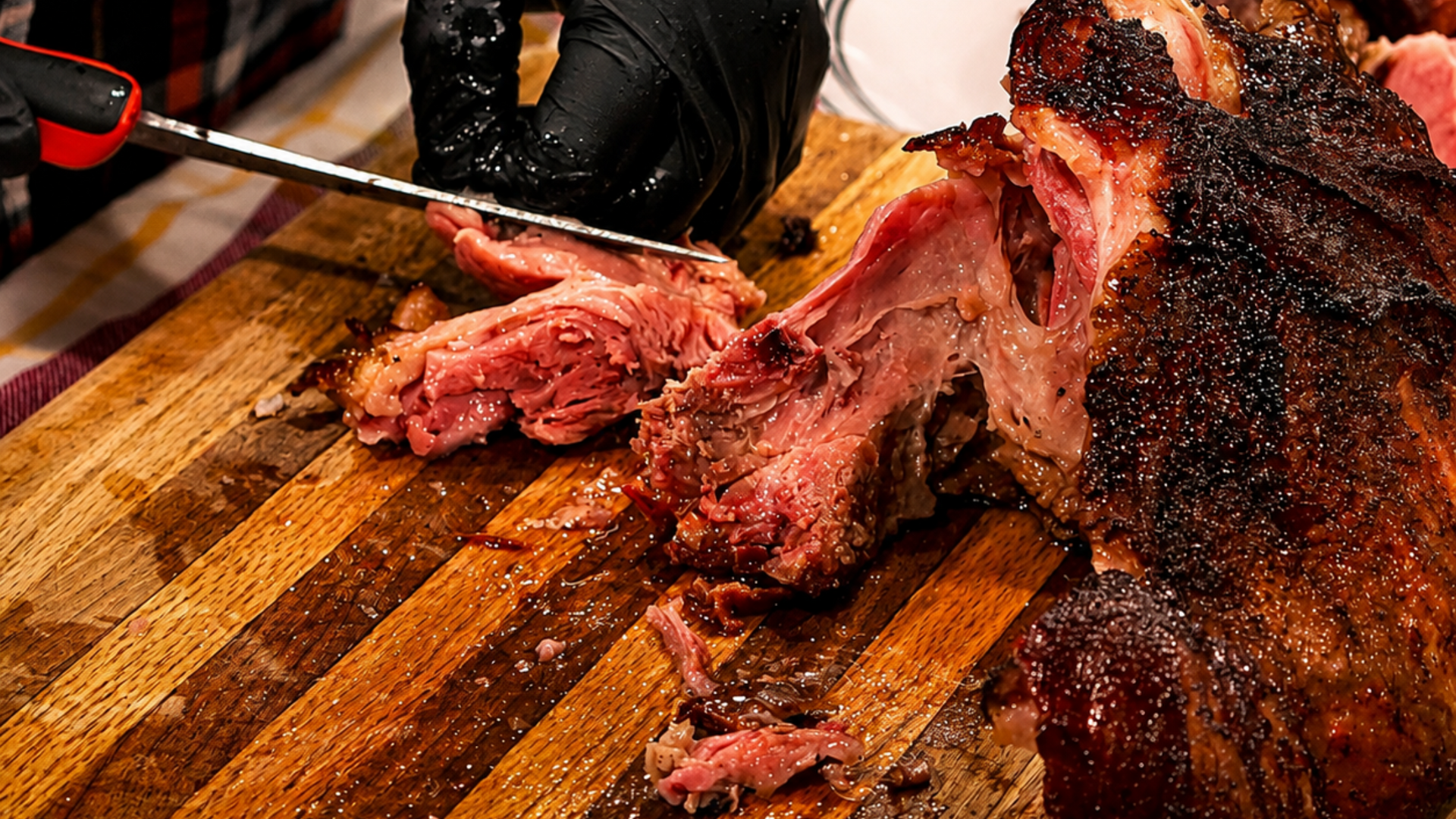 Gloved person carving a roast on a wooden cutting board beside a plate