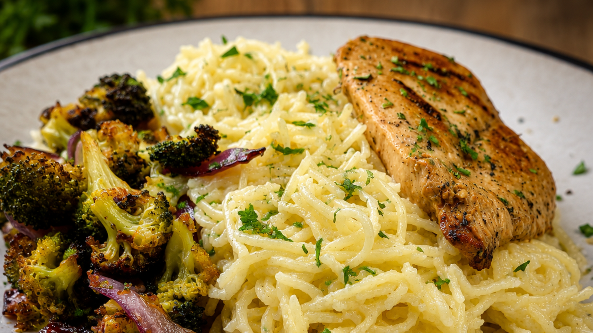 Plate of pasta with grilled chicken, broccoli, and red onion on a white dish