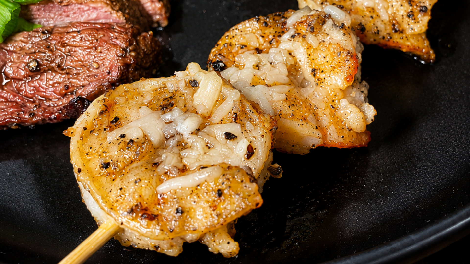 Grilled shrimp skewers and steak bites on a black plate