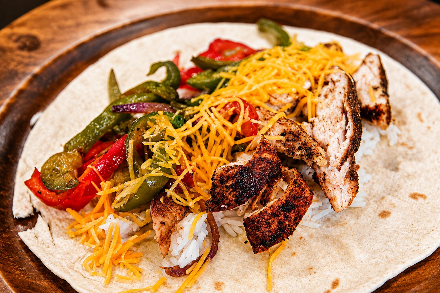 Grilled chicken taco with shredded cheese, peppers, and lettuce on a tortilla on a white plate