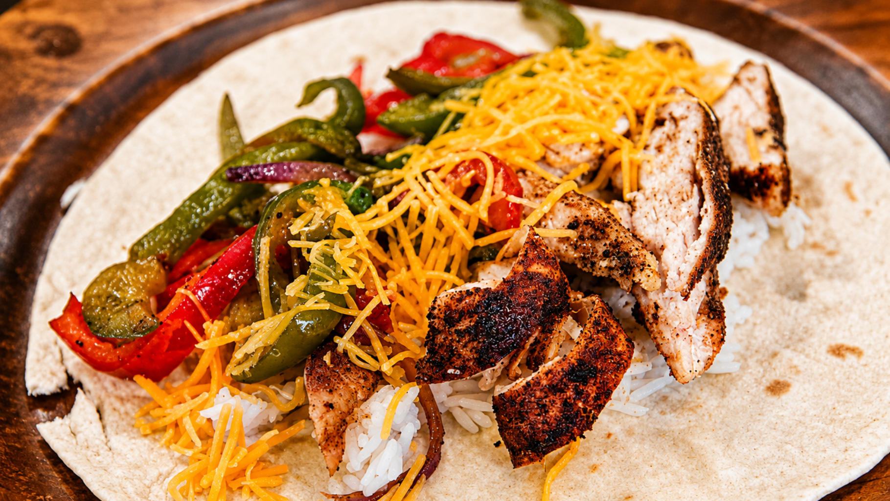 Grilled chicken taco with peppers, lettuce, and shredded cheese on a flour tortilla