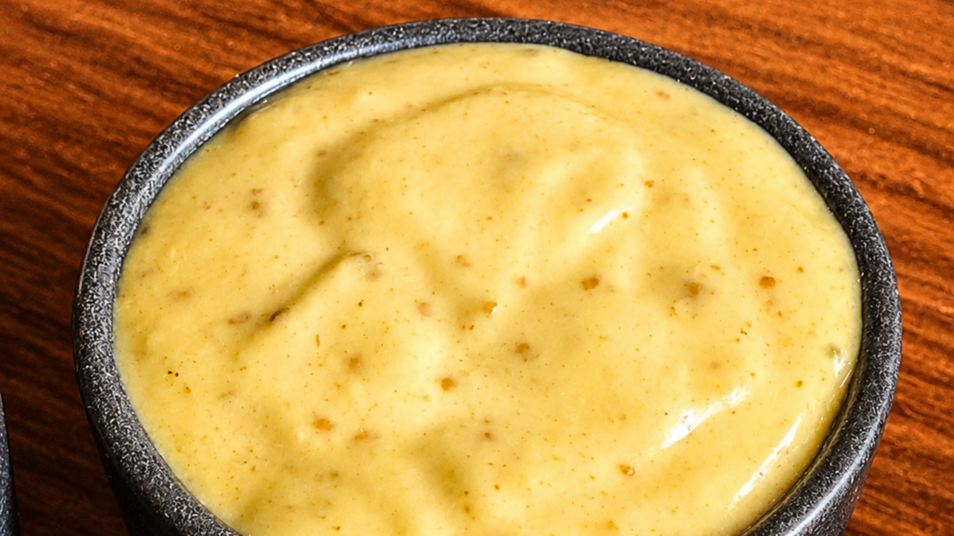Creamy yellow sauce in a small black bowl on a wooden surface
