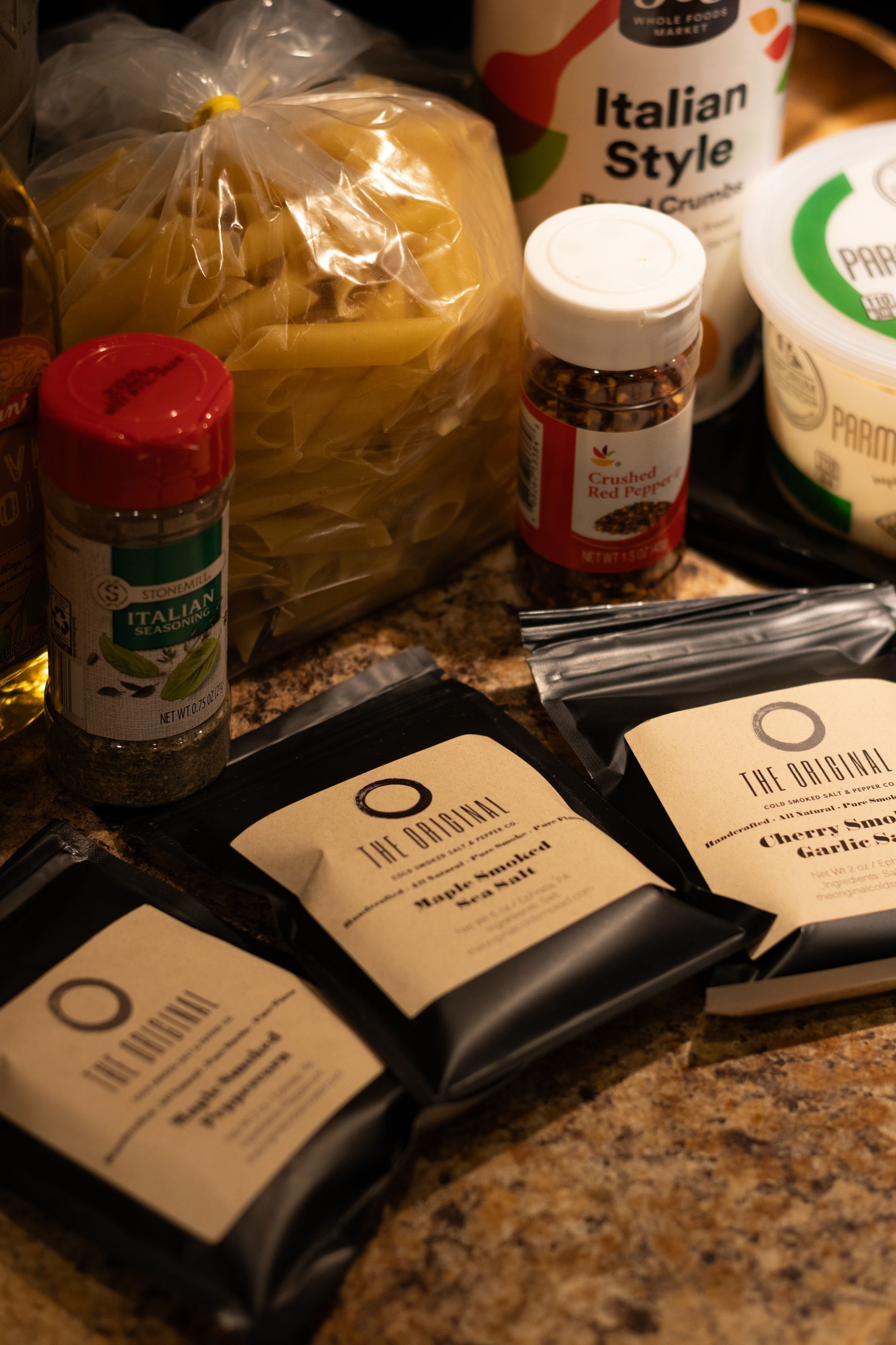 A bunch of spices are sitting on a counter next to a bag of pasta.
