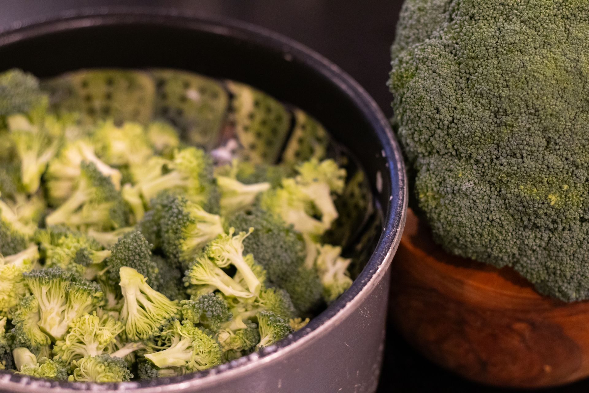A bowl of broccoli is sitting next to a head of broccoli.