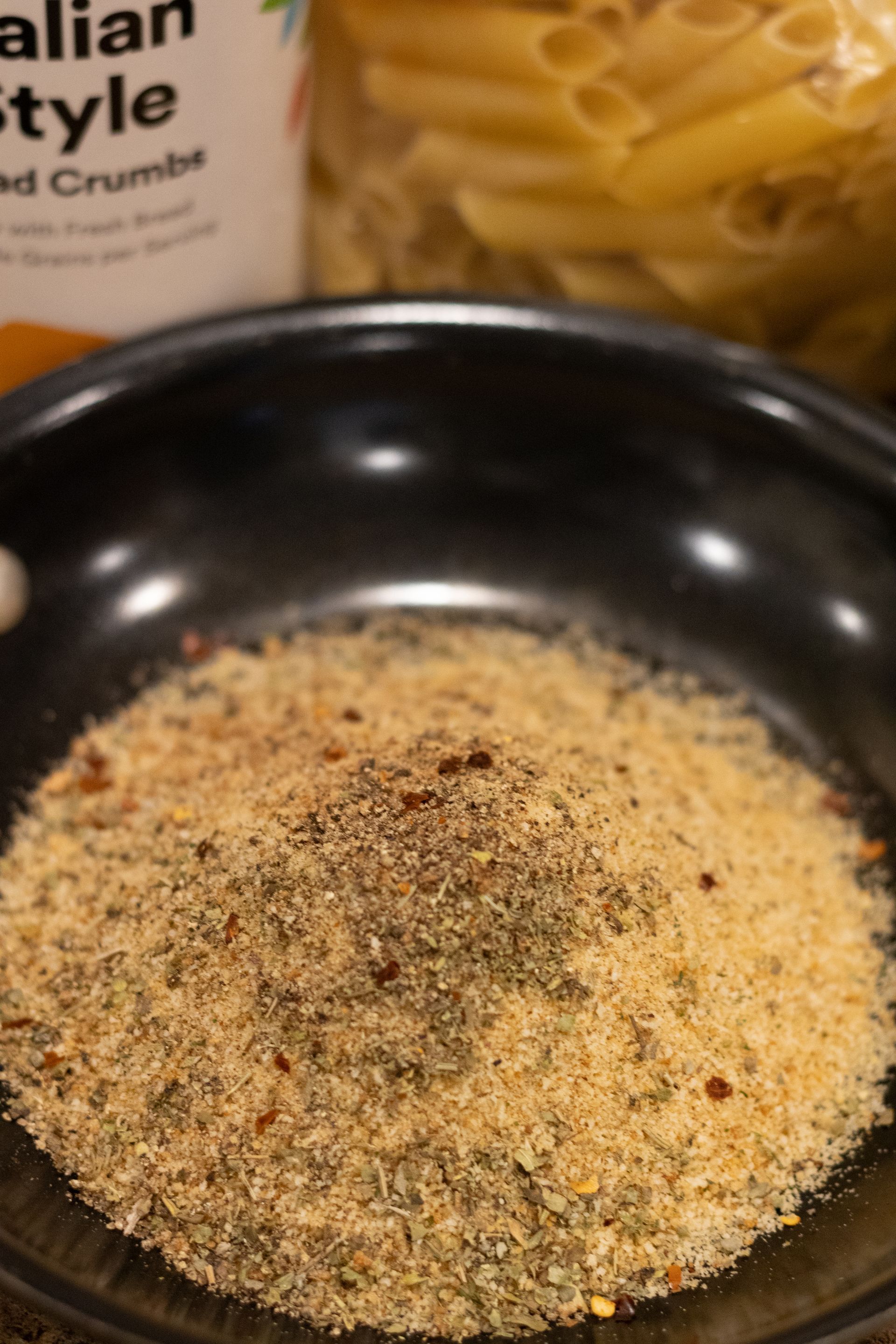 A bowl of bread crumbs next to a bag of pasta