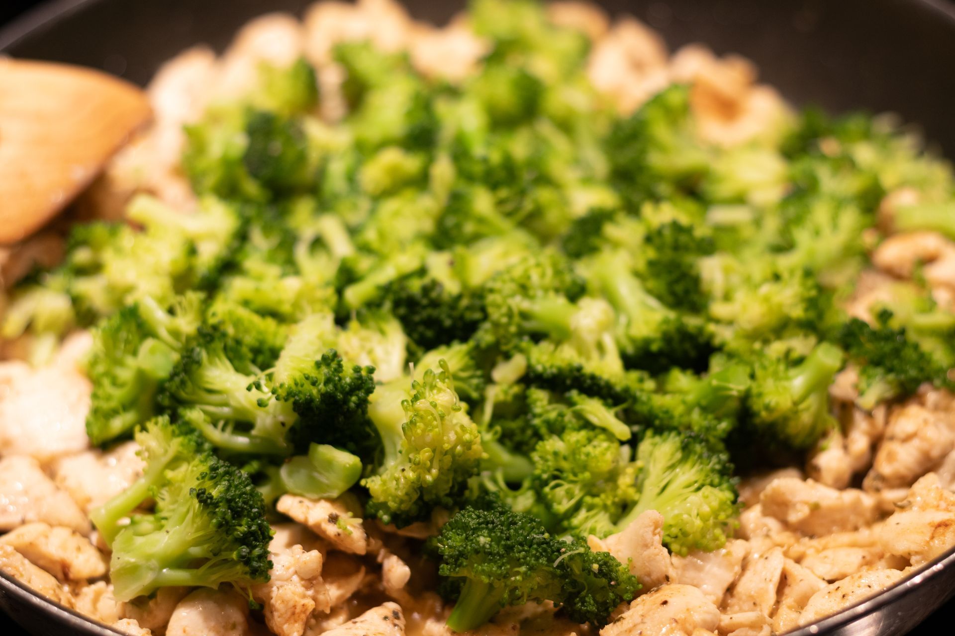 Broccoli and chicken are being cooked in a pan with a wooden spoon.