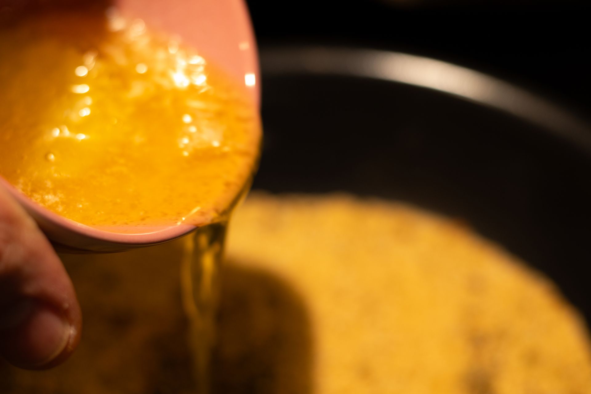 A person is pouring liquid from a measuring cup into a pot.