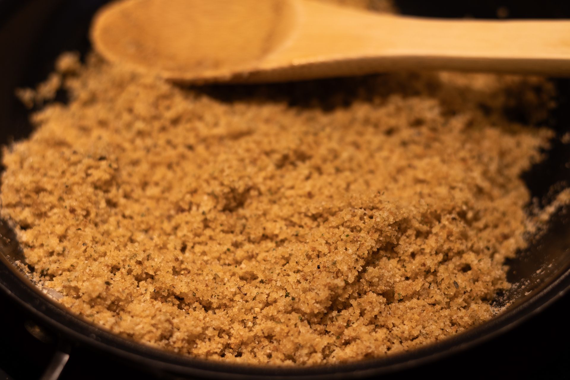 A wooden spoon is stirring a brown substance in a pan.
