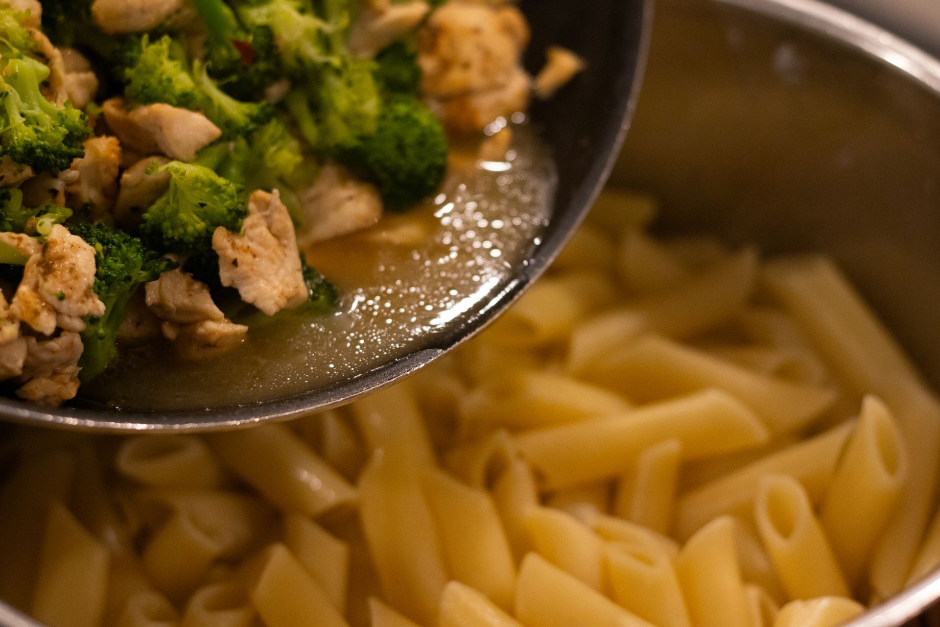 Broccoli and chicken are being poured into a pot of pasta.