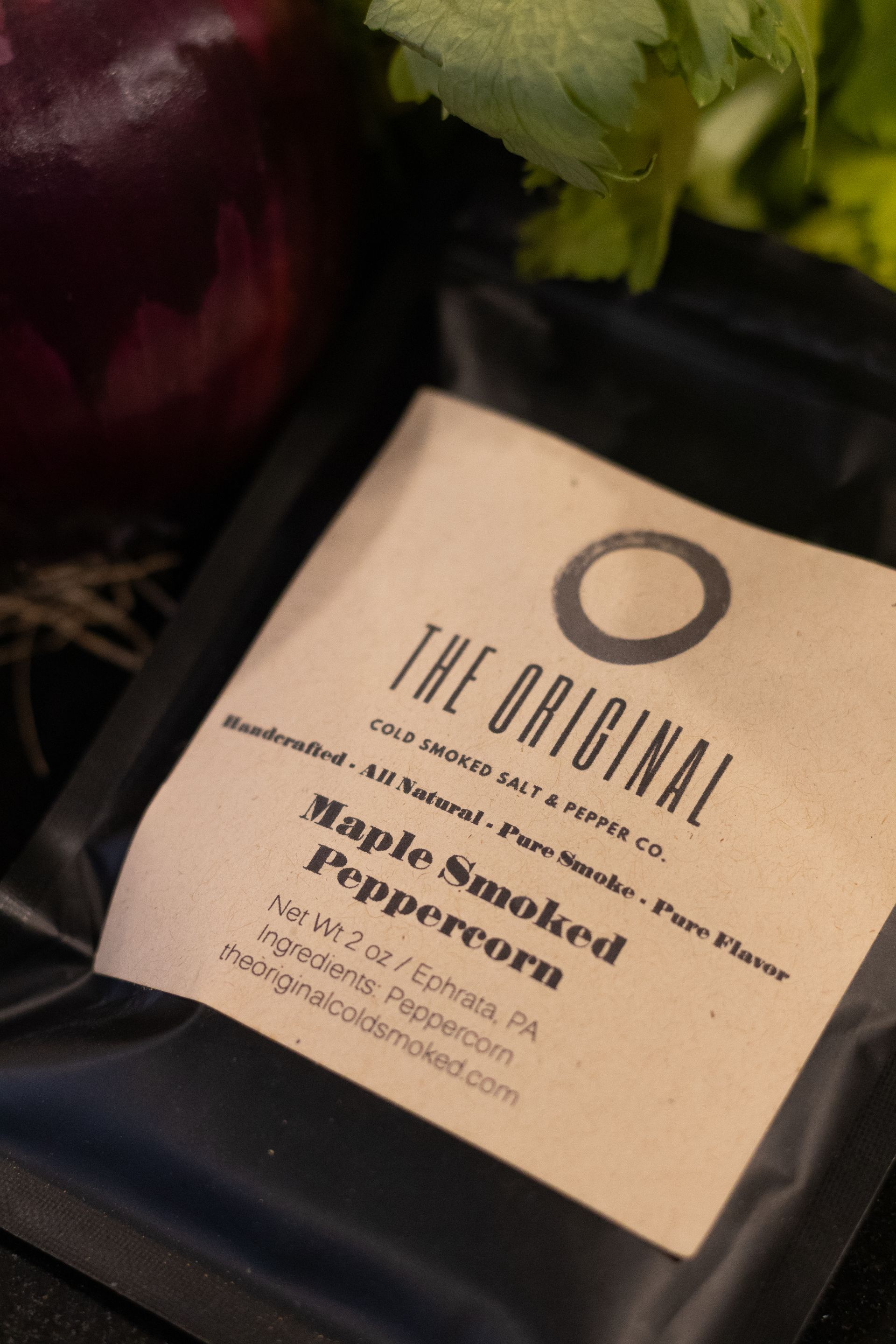 A bag of maple smoked peppercorn is sitting on a table next to vegetables.
