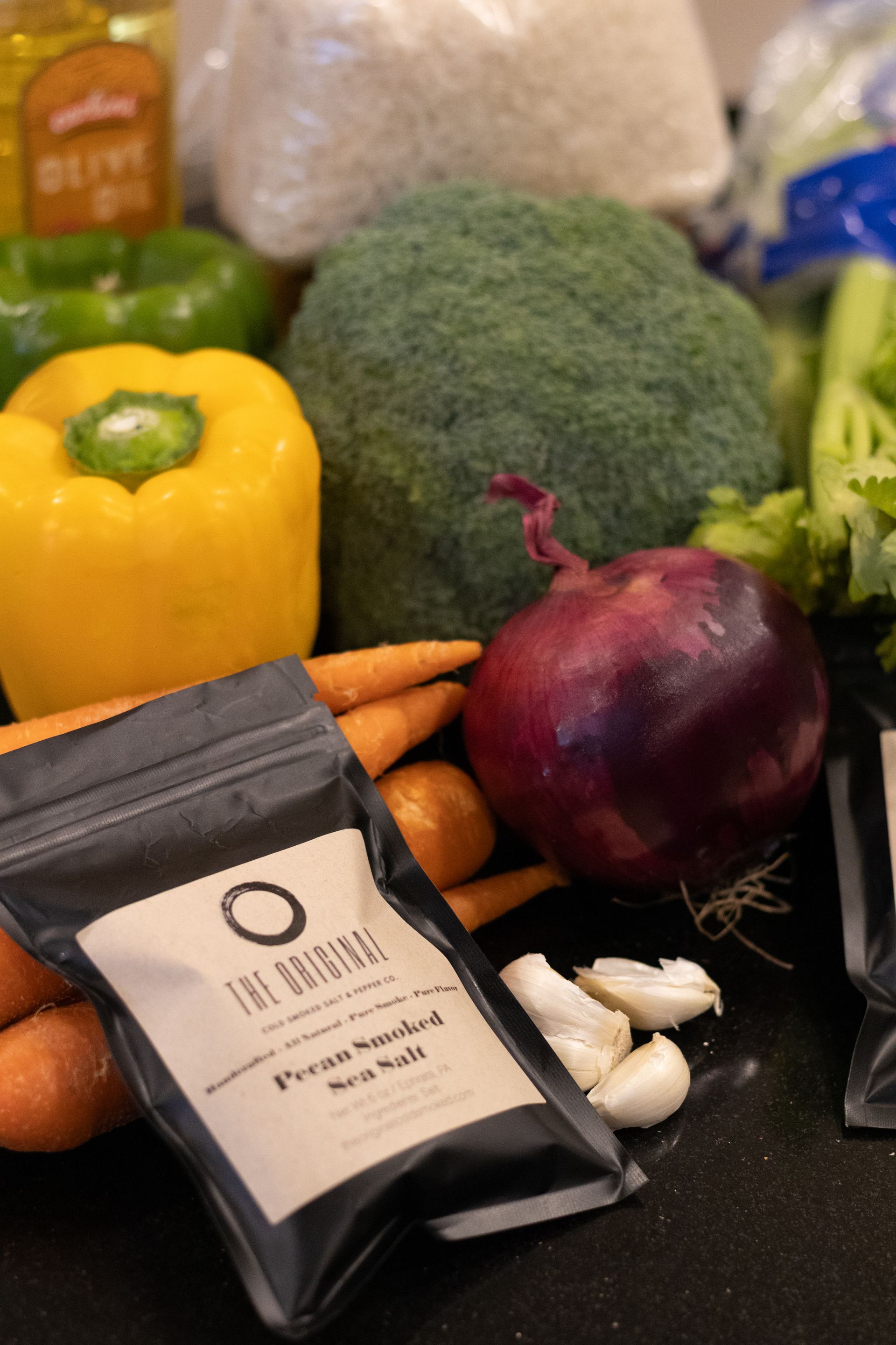 A variety of vegetables including broccoli carrots and peppers are on a counter next to a bag of the original