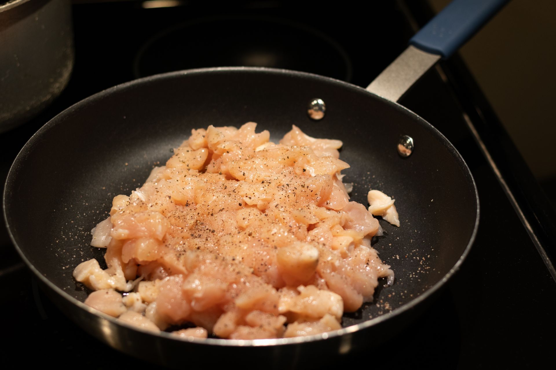 Chicken is being cooked in a frying pan on a stove