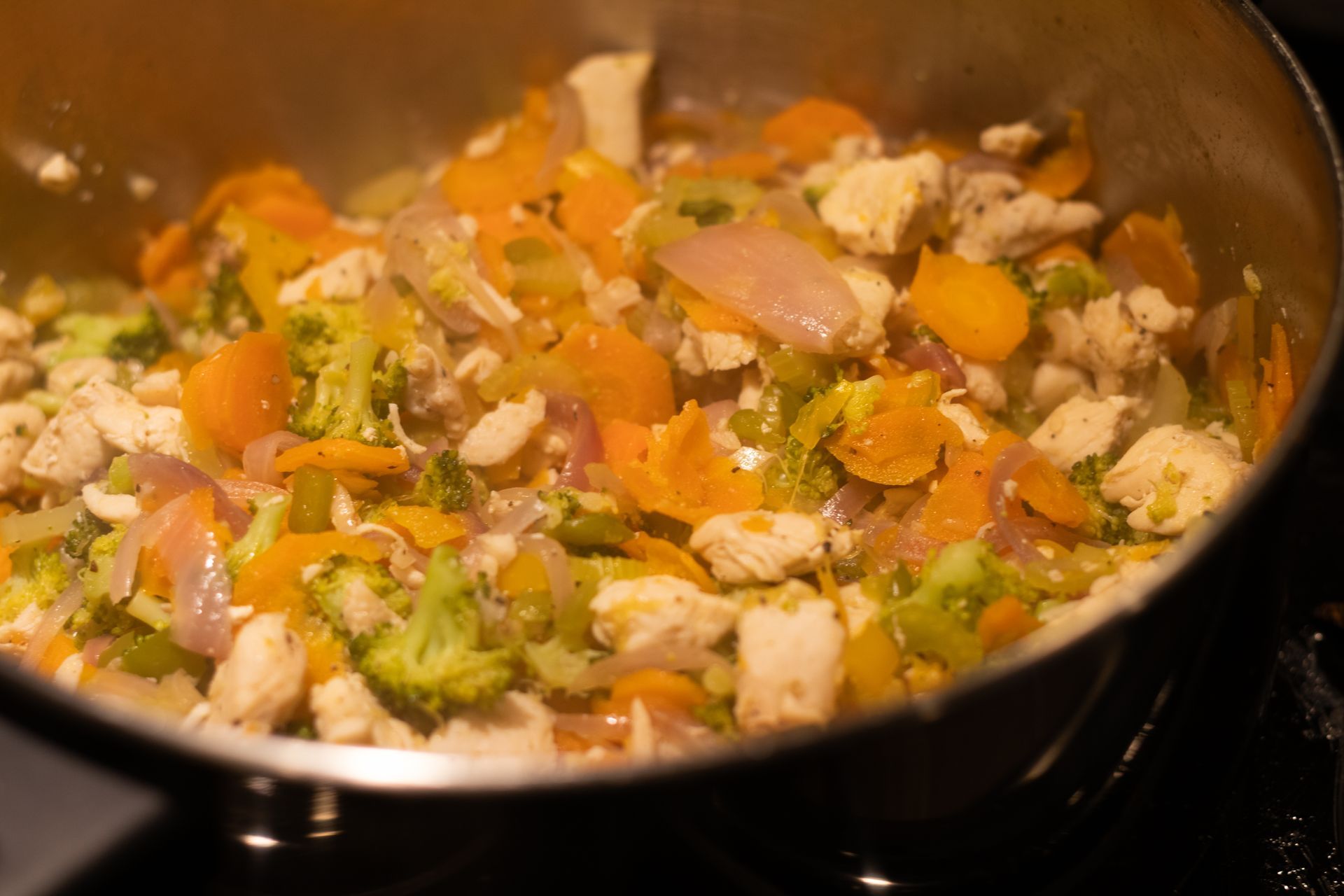 A pan filled with chicken and vegetables is cooking on a stove.