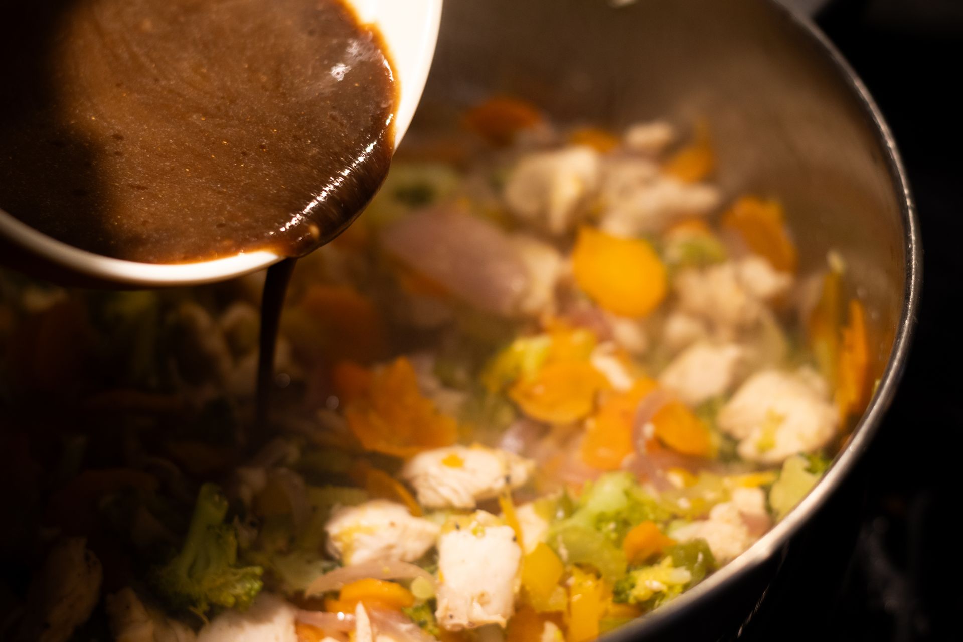 A person is pouring sauce into a pot of vegetables.