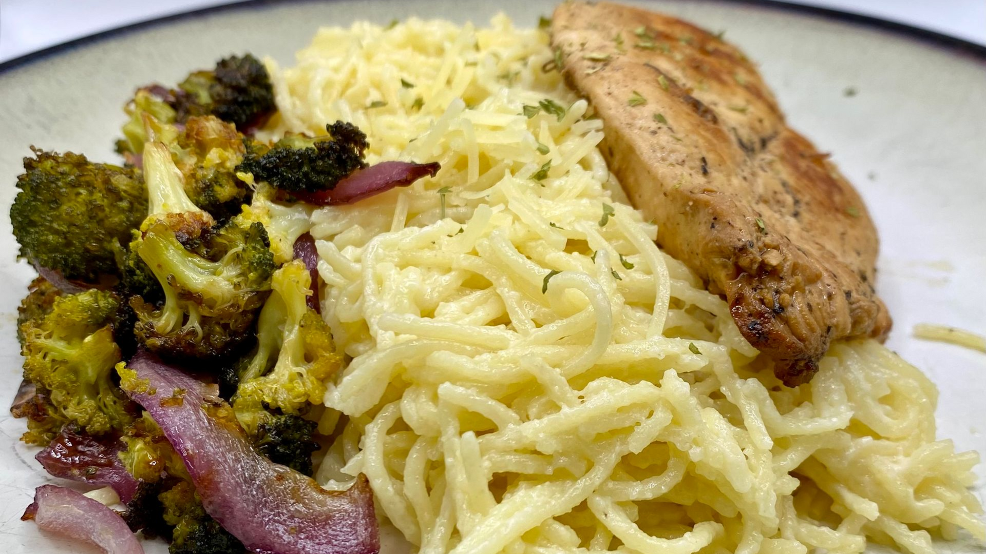 Plate with roasted broccoli and red onion, pasta, and chicken breast.