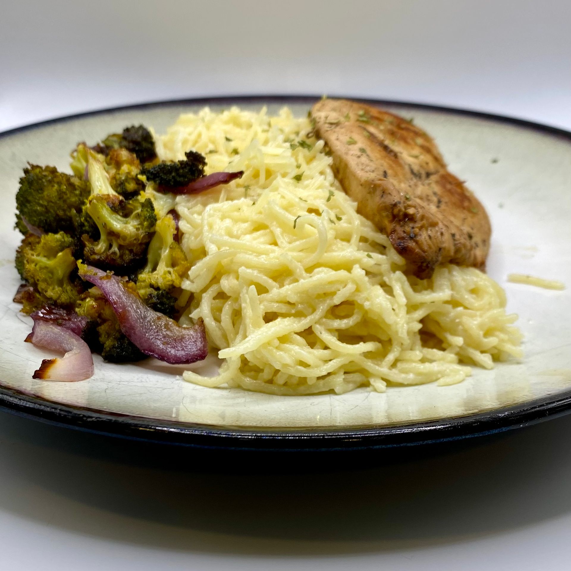 Plate with spaghetti, roasted broccoli and red onion, and a grilled chicken breast.