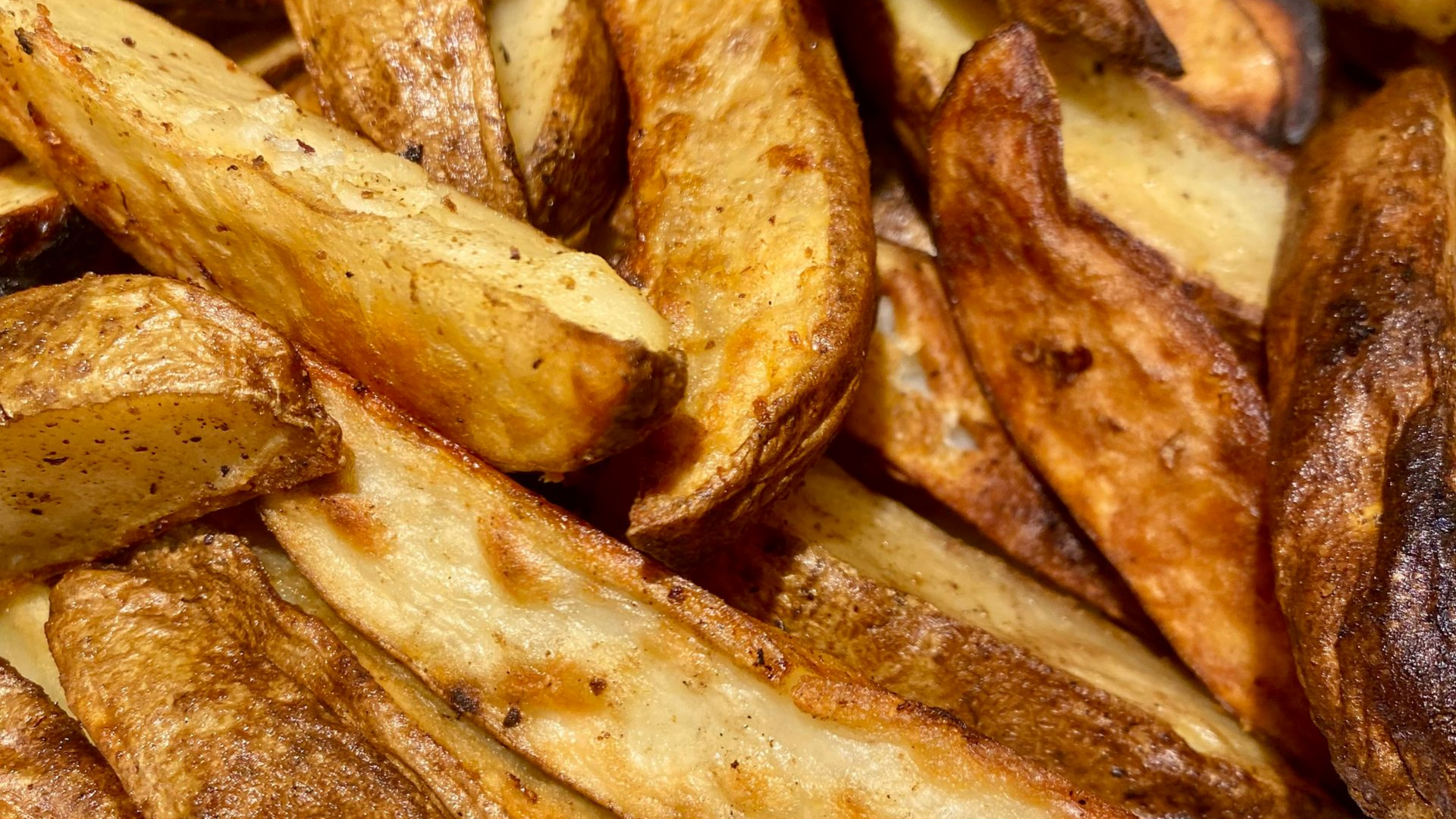 Close-up of crispy, golden-brown potato wedges seasoned with spices.