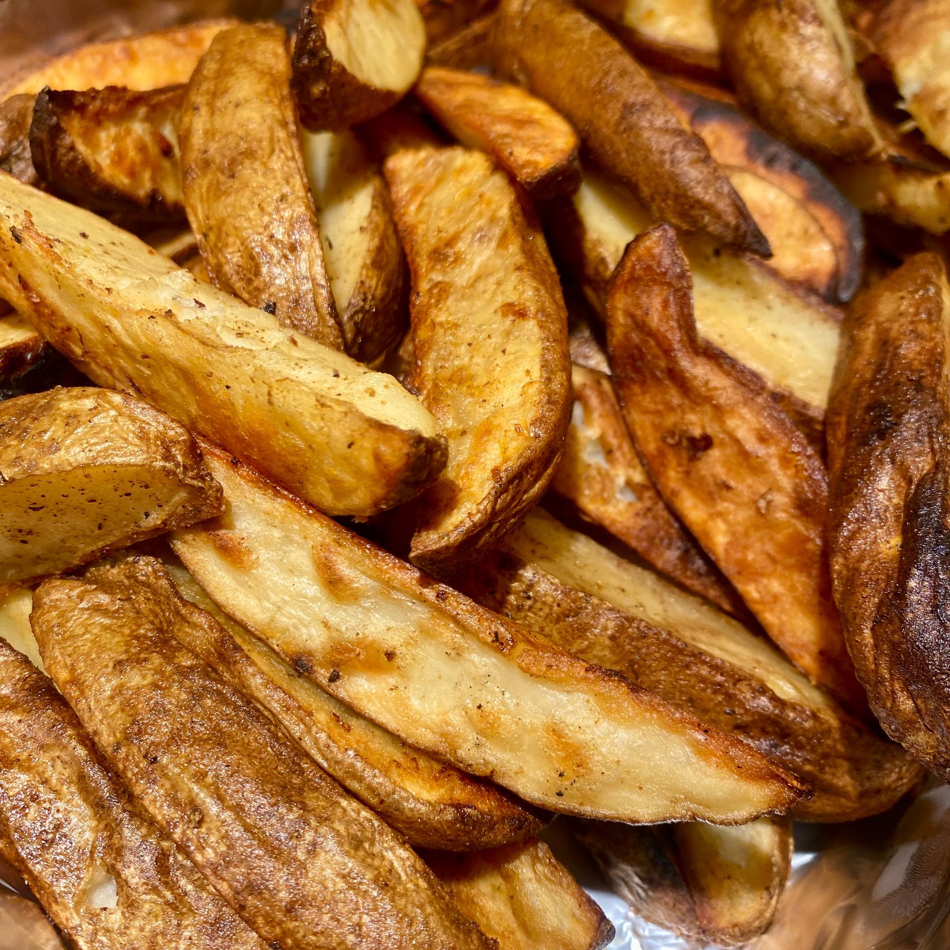 Close-up of golden-brown potato wedges, some slightly charred, piled in a bowl.