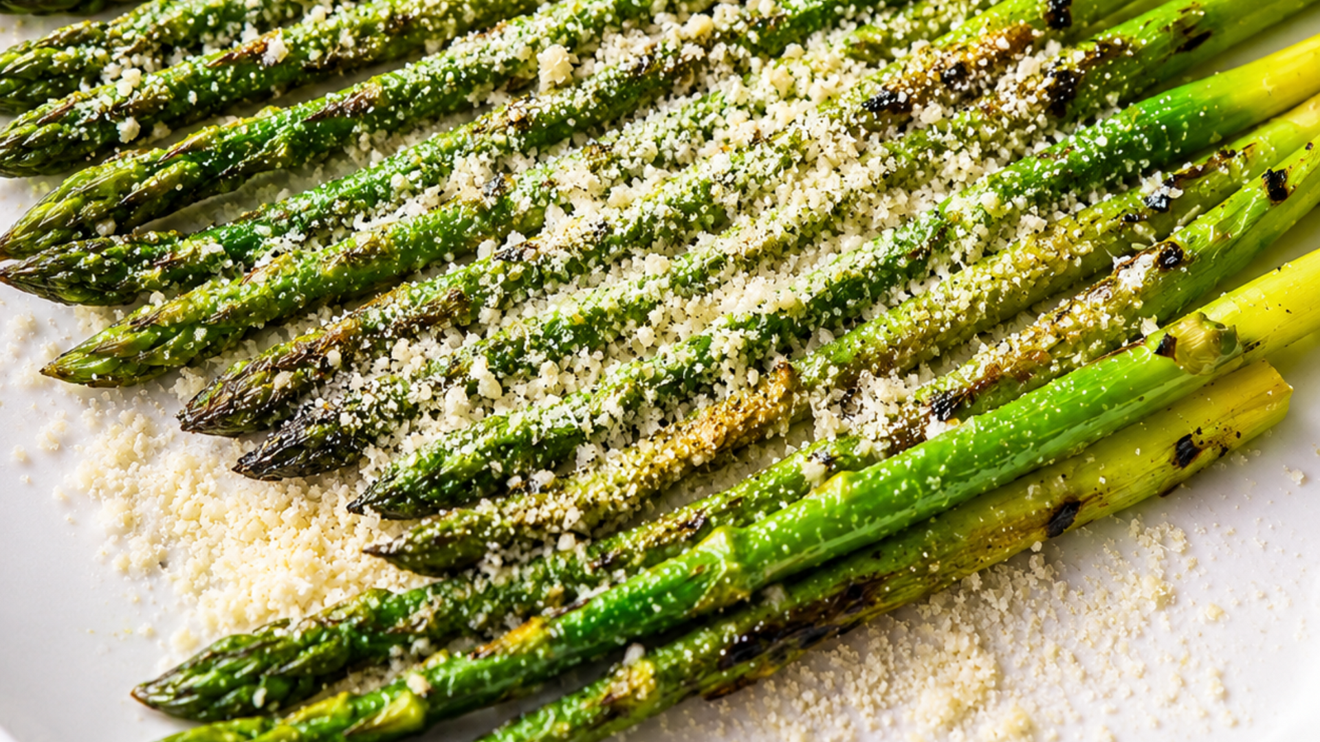 Grilled asparagus spears topped with grated cheese on a white plate