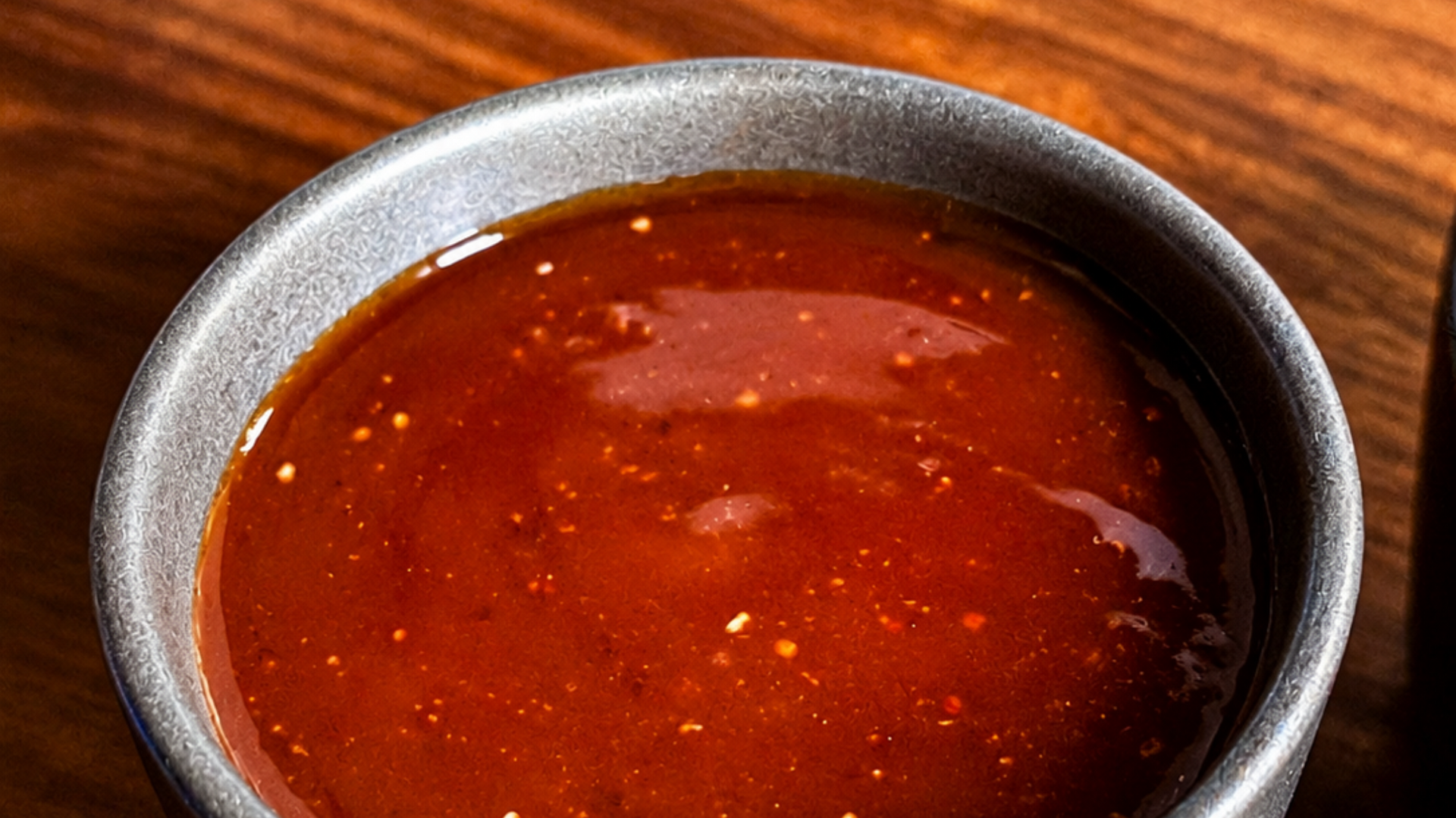 Close-up of a bowl of glossy red sauce or soup with a metal rim