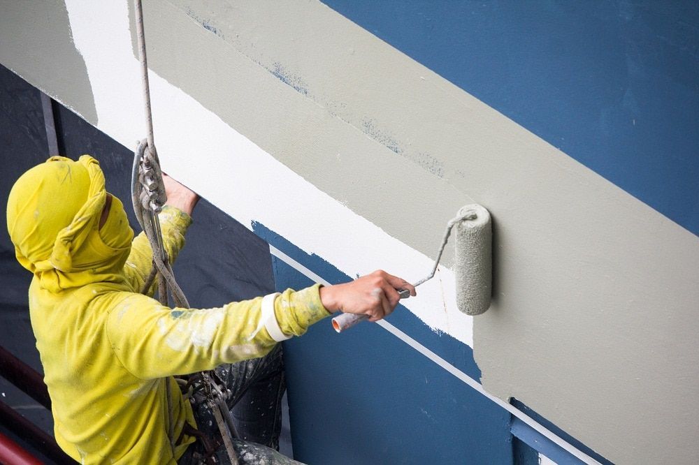 Person in a yellow raincoat painting a blue and white wall with a roller.