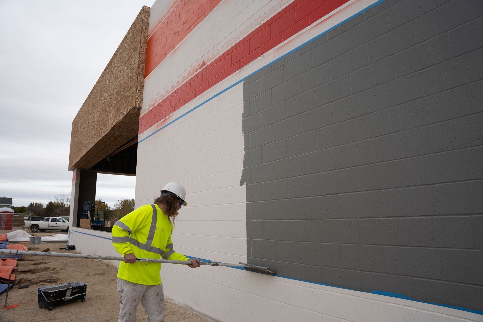 Worker in a neon safety jacket painting a large building wall outdoors.