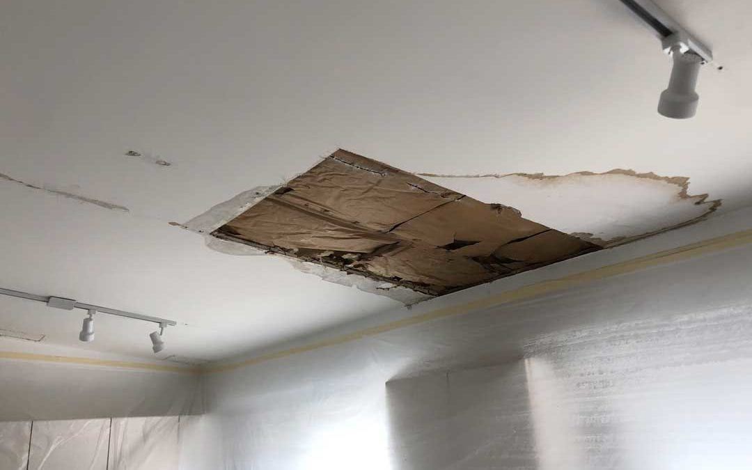 Ceiling with a large damaged hole and exposed brown insulation or backing material