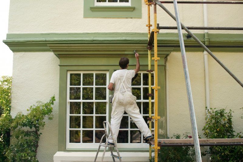 Worker on ladder painting the exterior of a house beside a window and scaffolding