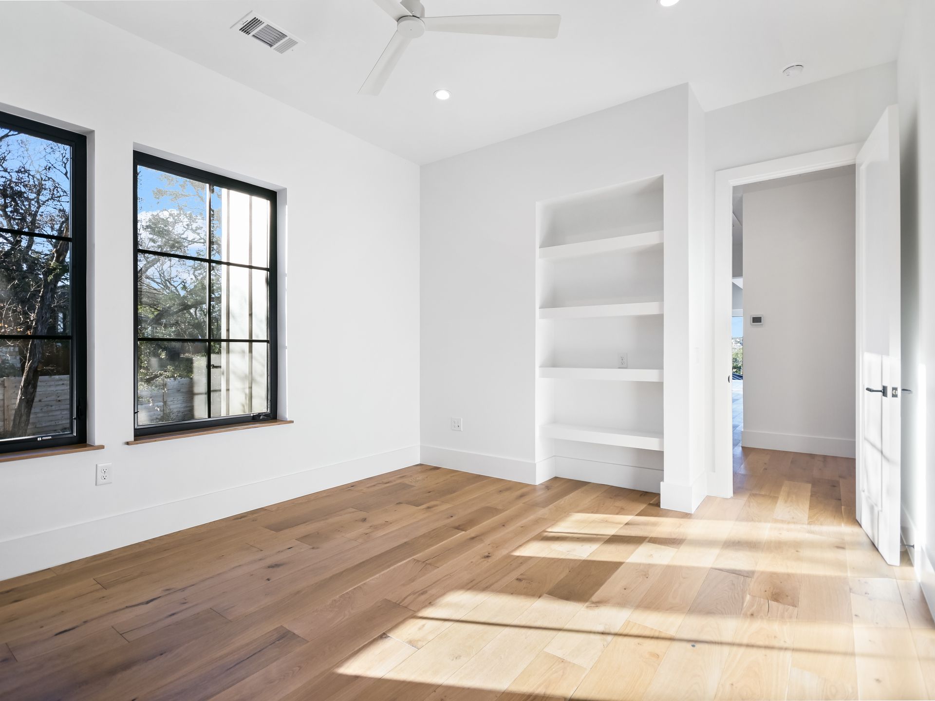 An empty room with hardwood floors and a ceiling fan.
