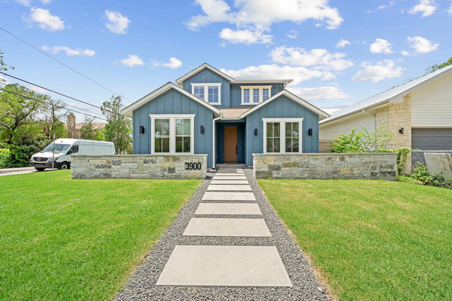 Blue house with white trim, stone wall and walkway, and green lawn under a blue sky.