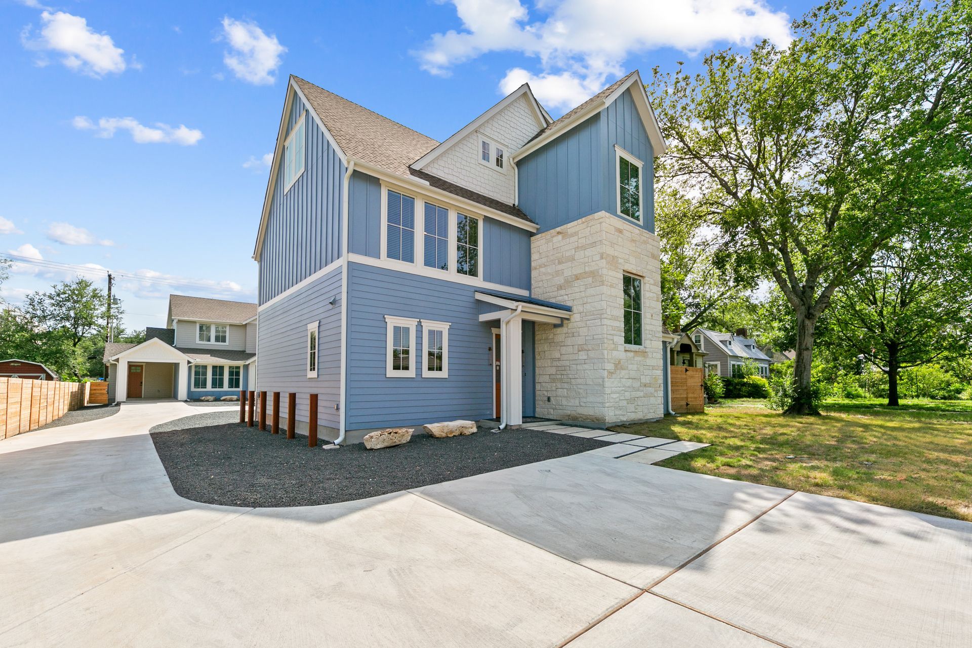 Modern two-story house with light blue siding, stone accent, and concrete driveway on a sunny day.
