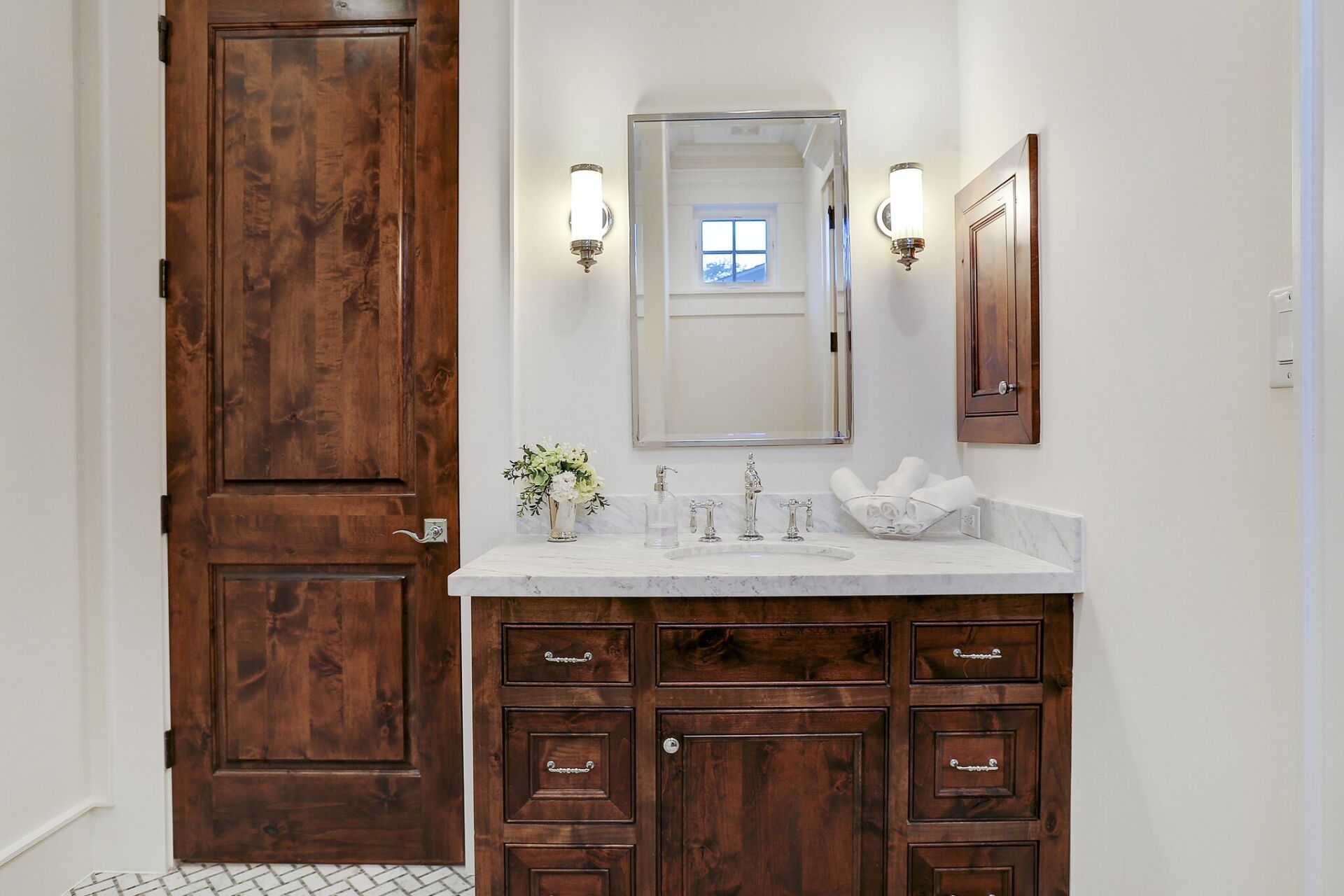 A bathroom with a sink , mirror and wooden cabinets.