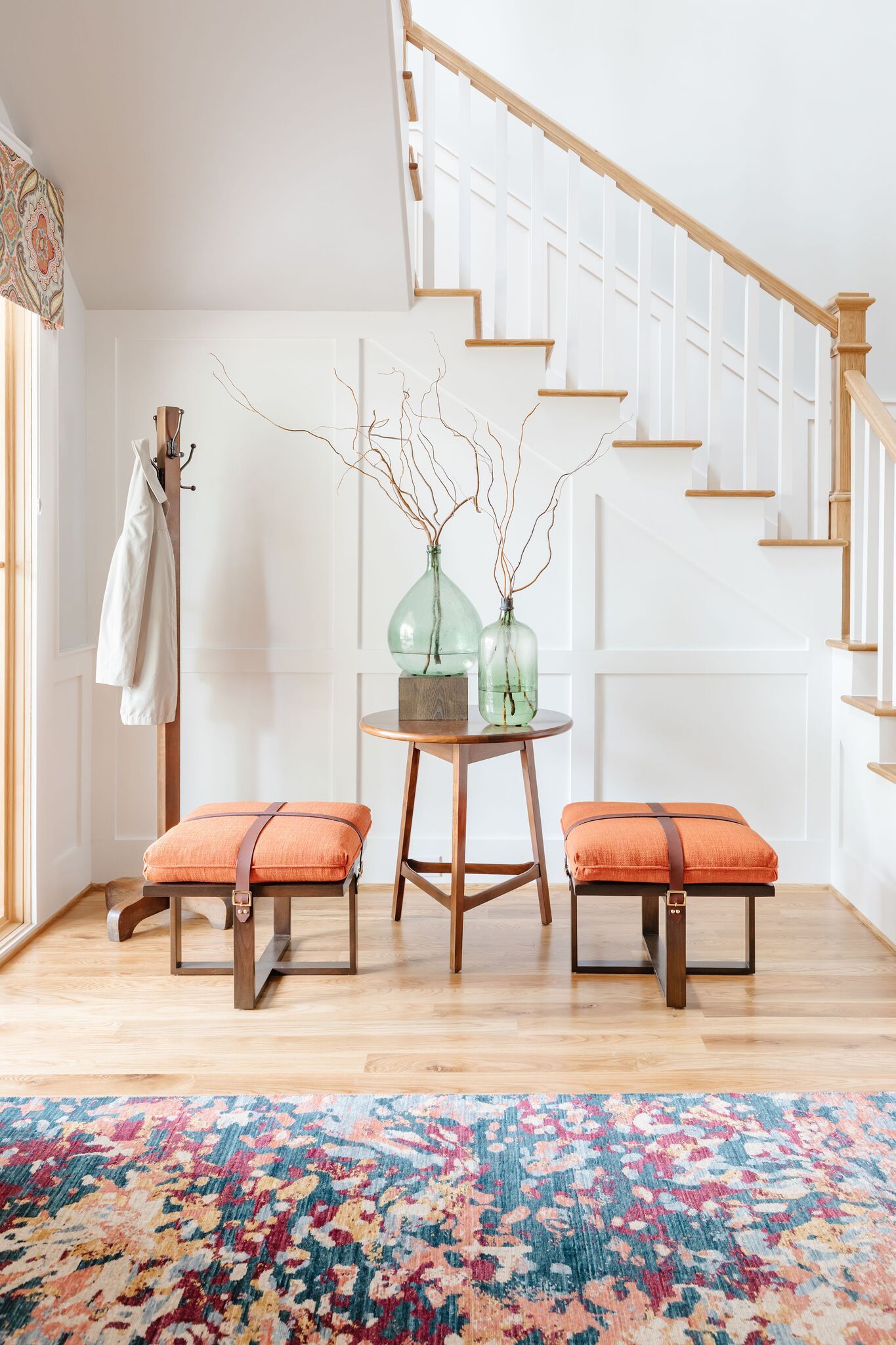 A hallway with stairs , ottomans , a table and a rug.