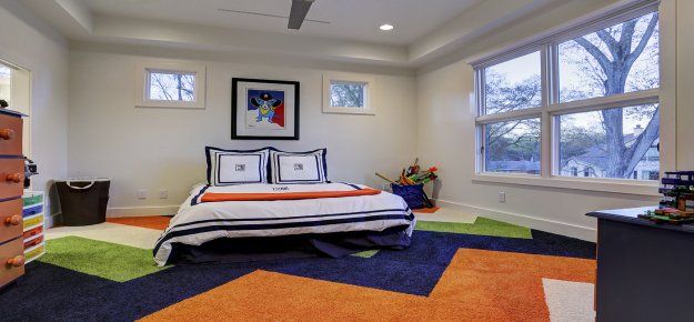 A bedroom with a bed , dresser , window and colorful rug.