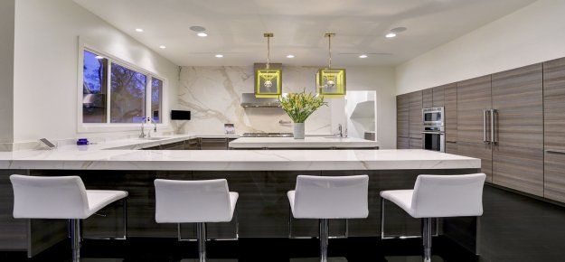 A kitchen with a large island and three white chairs.