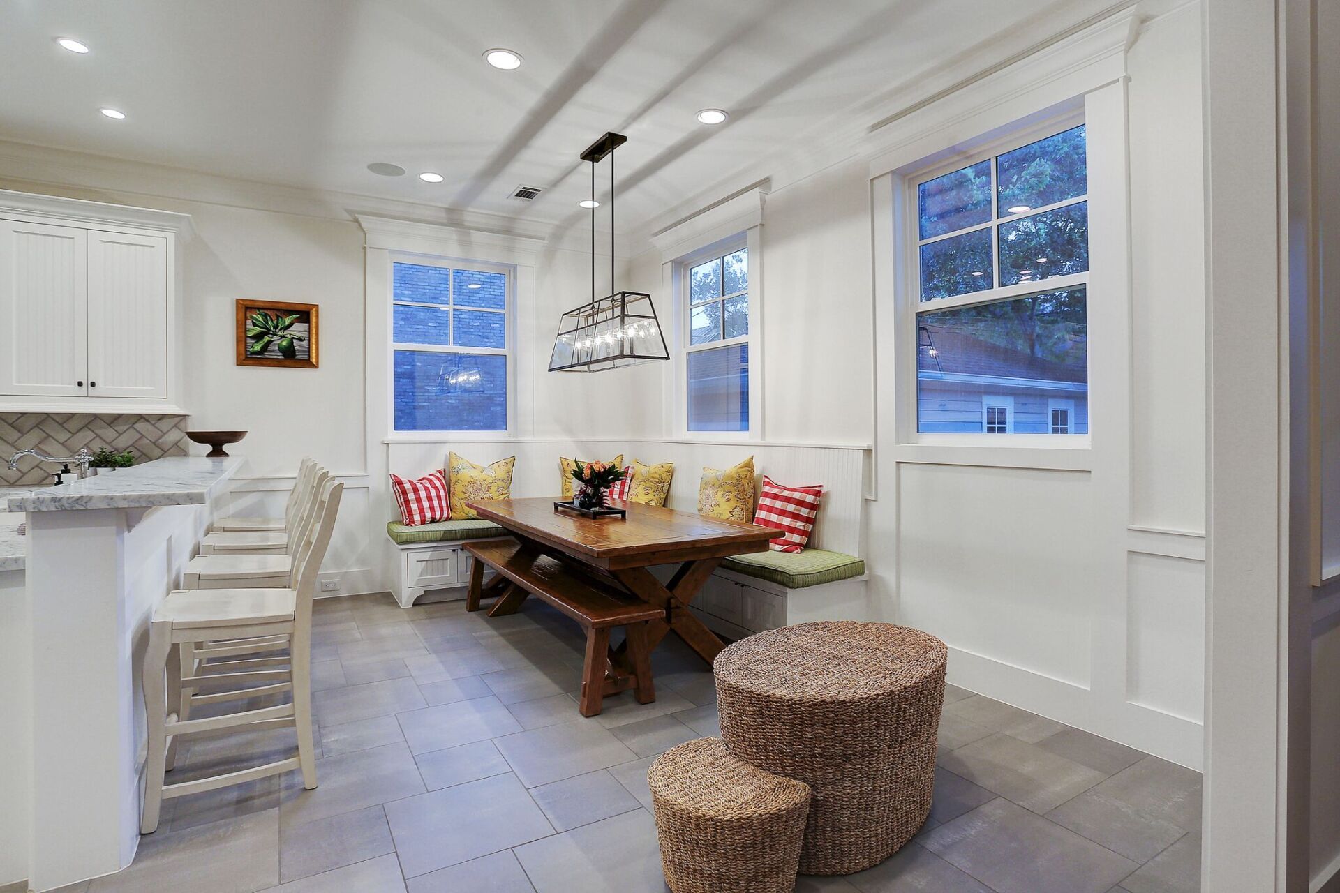 A dining room with a table and benches and wicker ottomans.