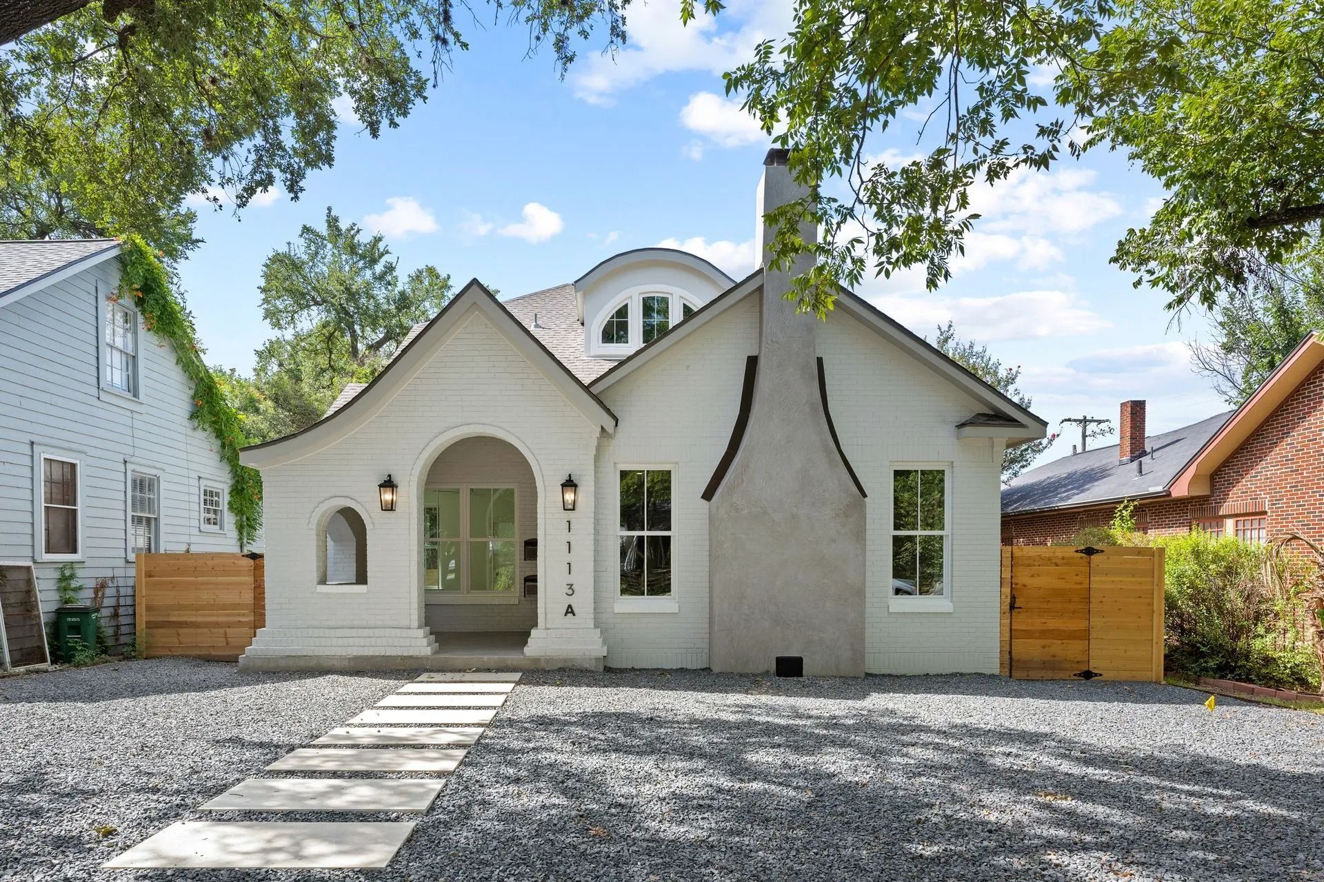 White stucco house with arched doorway, path, gray gravel, and wooden fences.