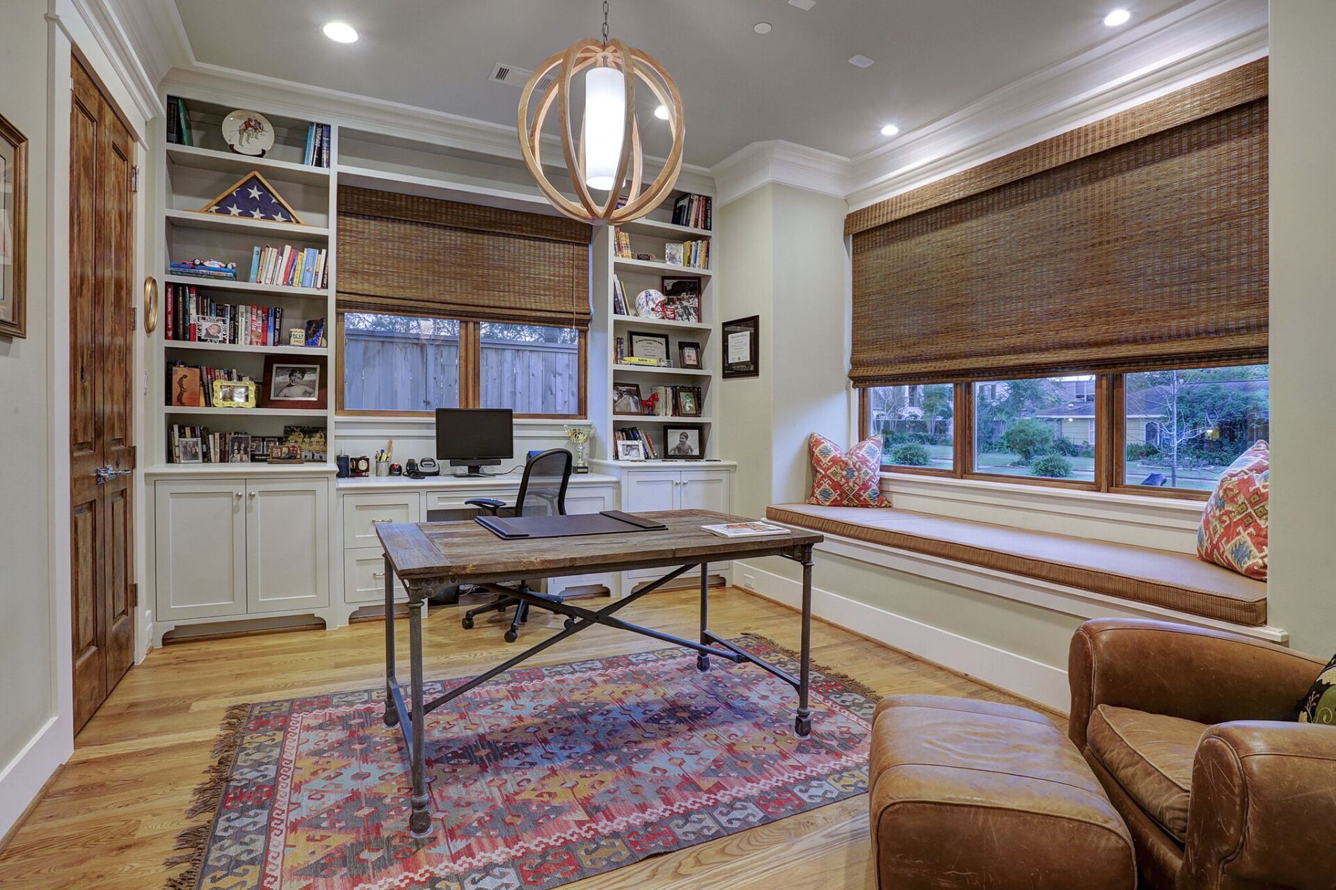 There is a desk in the middle of the room with a window seat.